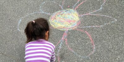 Et barn tegner en fin blomst med kridt på asfalt