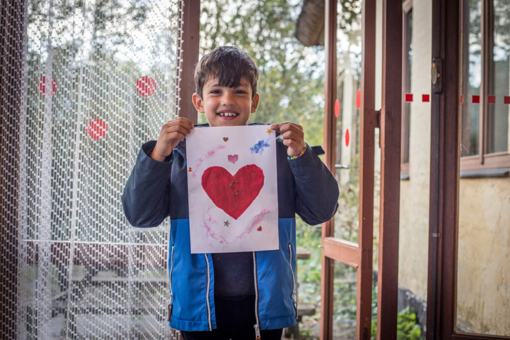 Smilende dreng viser en tegning af et hjerte frem, som han har lavet på kolonien